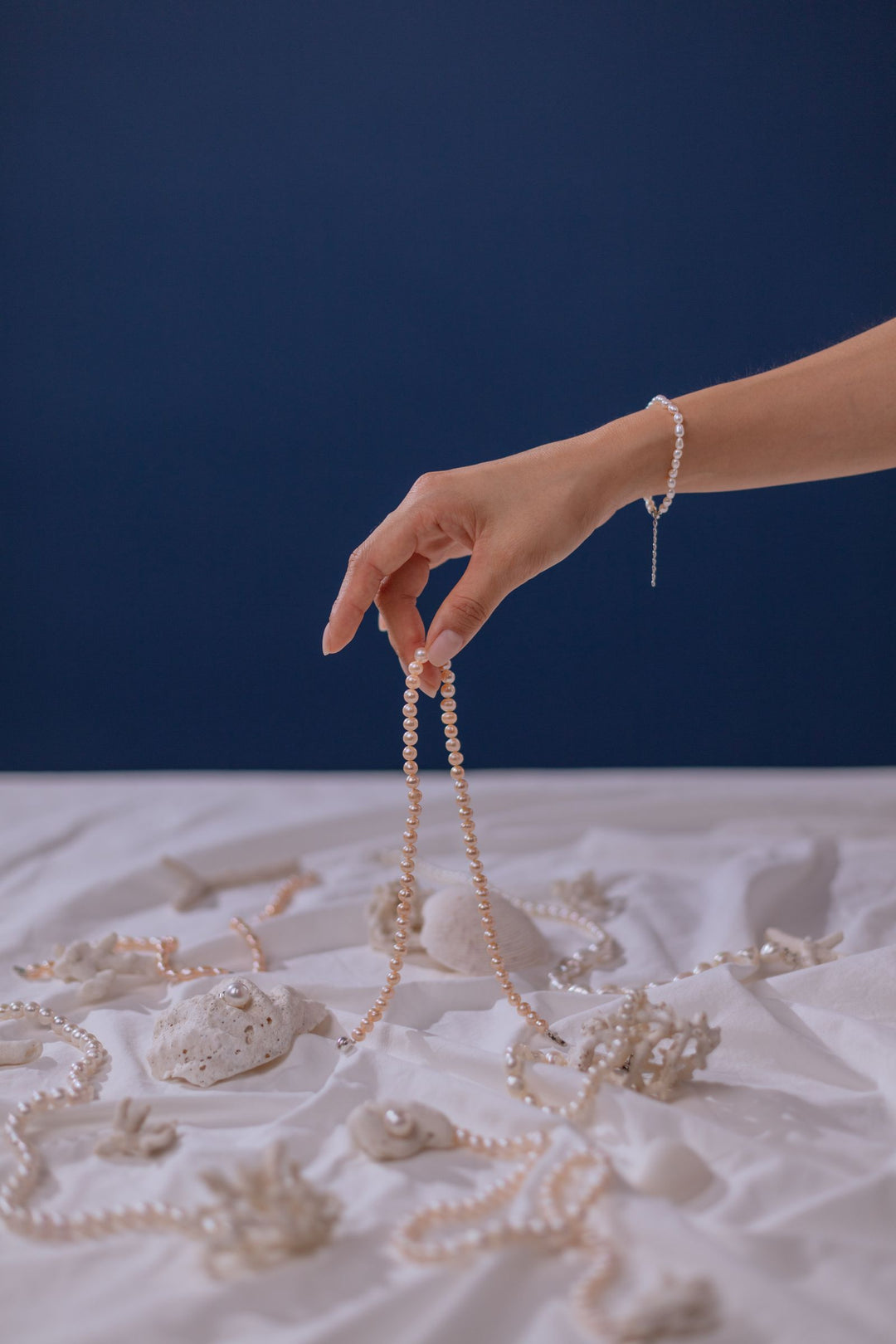 Hand examining a white pearl necklace on soft fabric